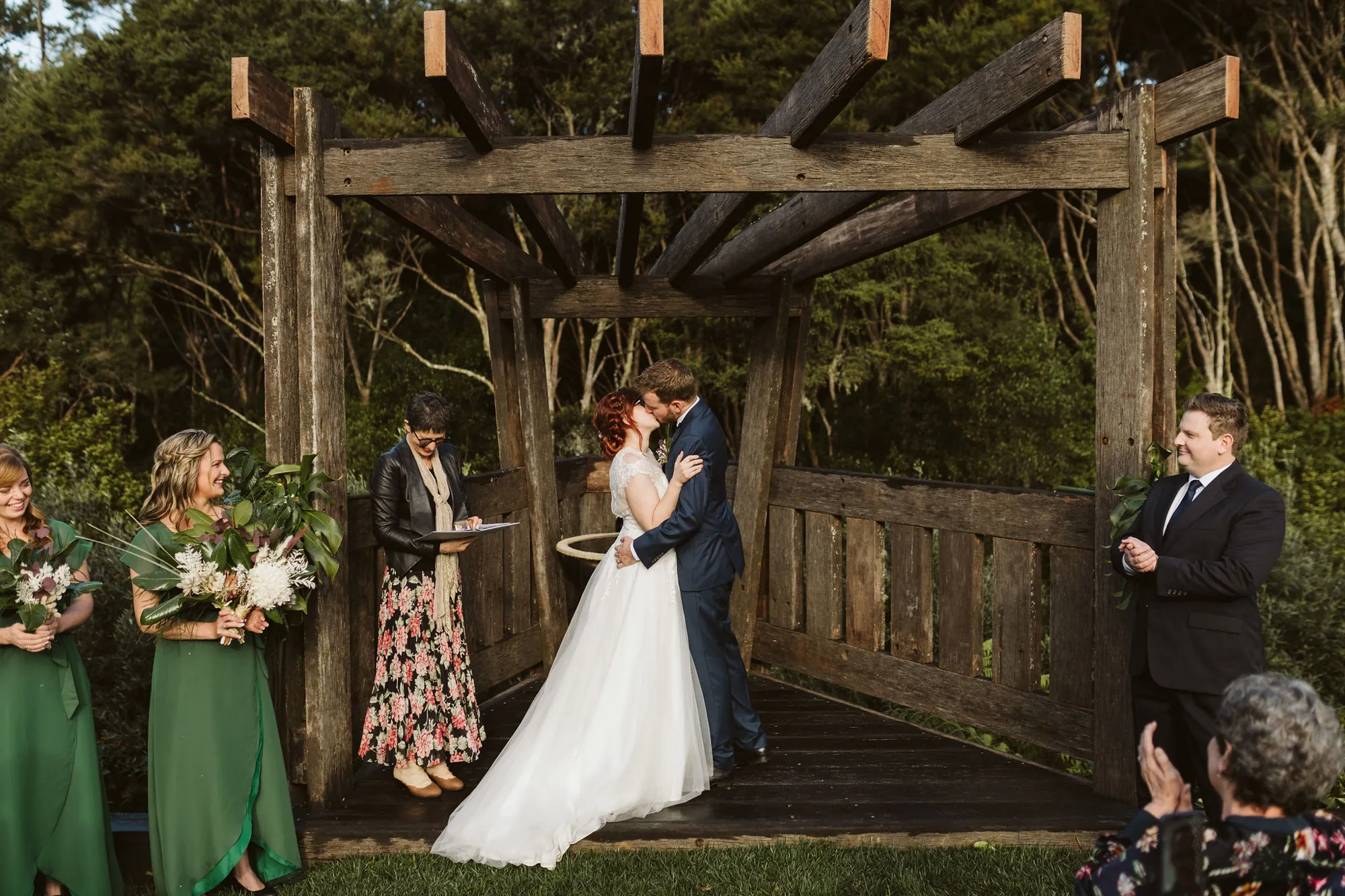Amy and Vince kissing at the end of their ceremony under a rustic timber pergola