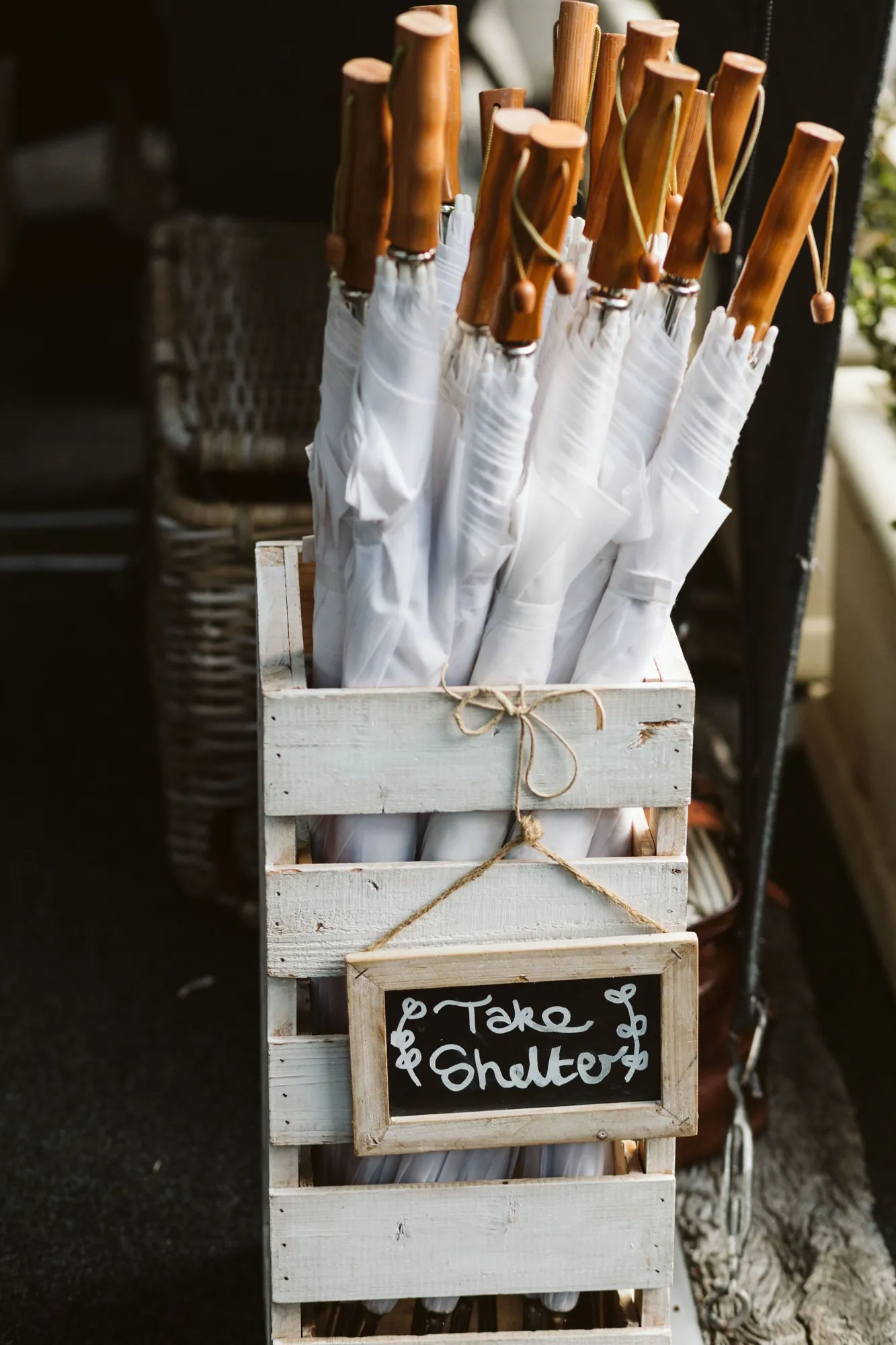 White wedding umbrellas in a wooden crate with a chalkboard sign reading Take Shelter