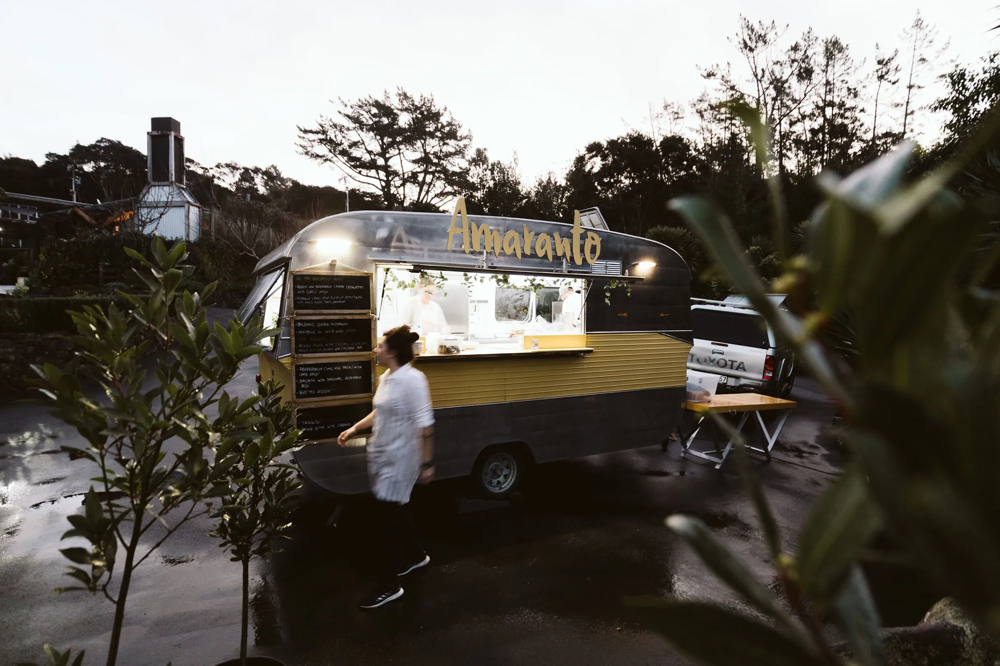 The Amaranto Pasta & Cucina caravan lit up at dusk with the menu on chalkboards