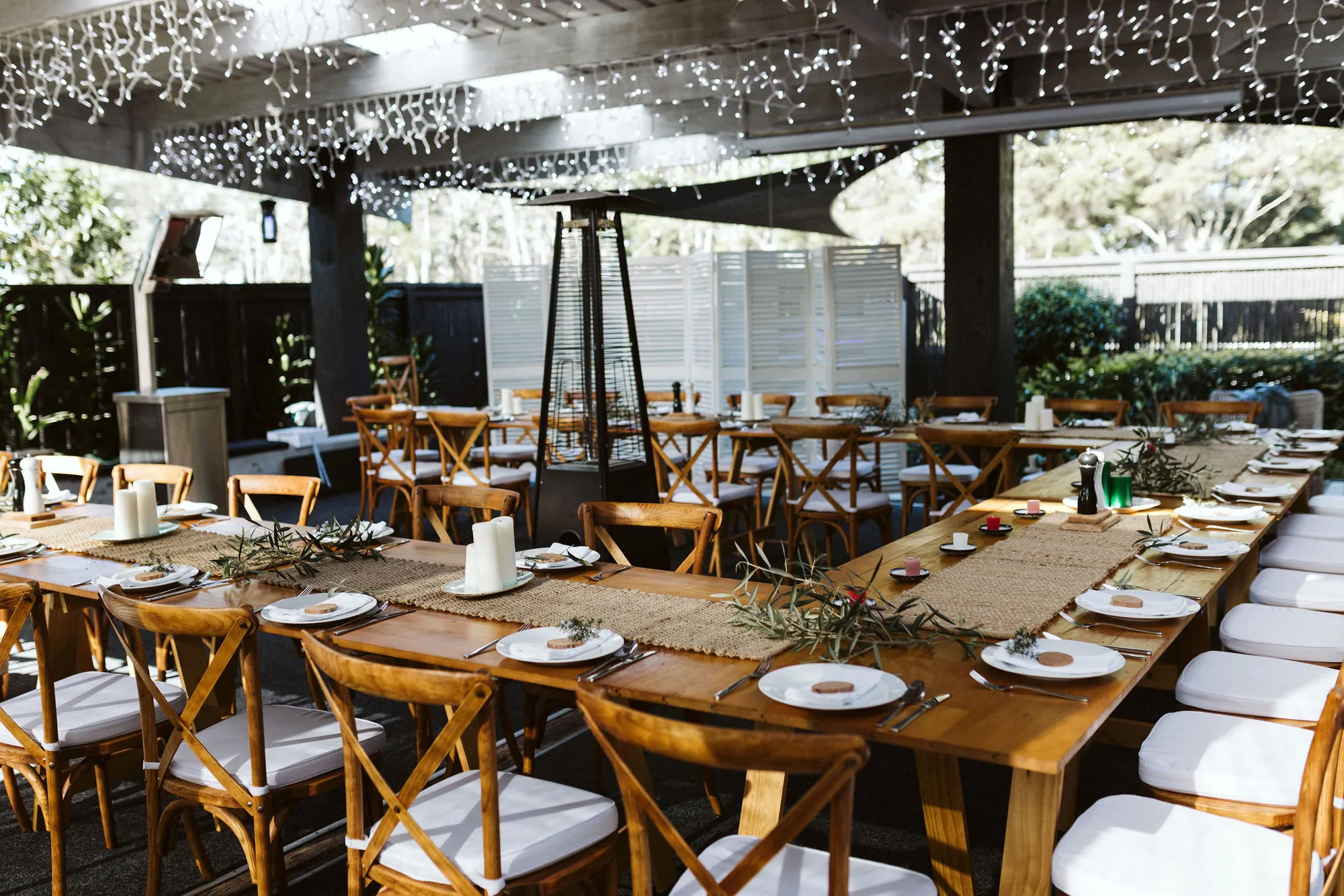 Long wooden tables set under fairy lights with olive branches and white candles