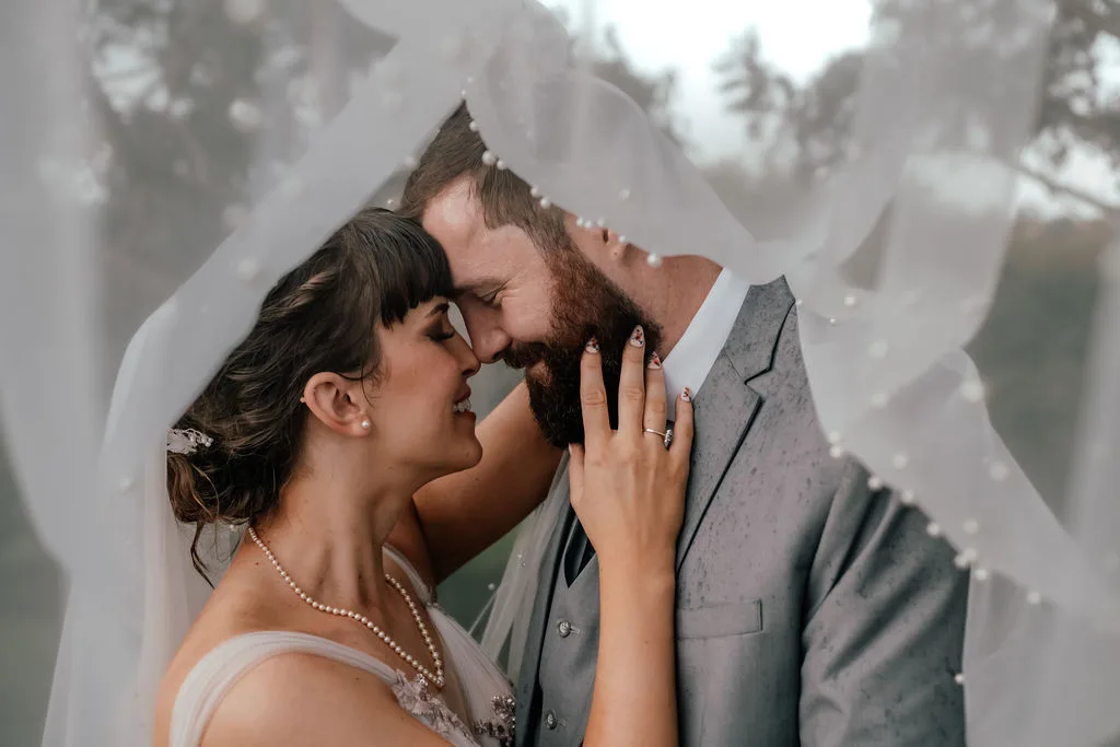 Andrew and Laura share their first kiss under the rustic amber flower arch at their ceremony at Waterfall Farm