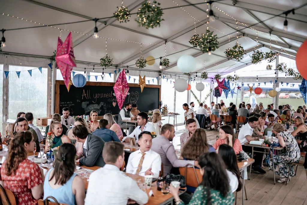 The full wedding marquee at Waterfall Farm filled with guests, pink blue and gold star lanterns hanging from the rafters