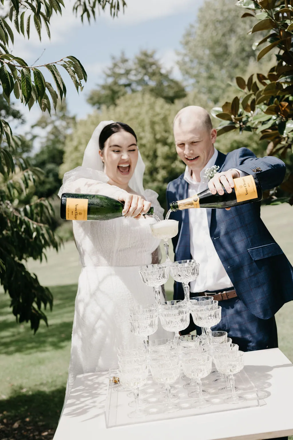 Chloe and Mitchell laughing as they pour champagne down the tower at their Matakana wedding