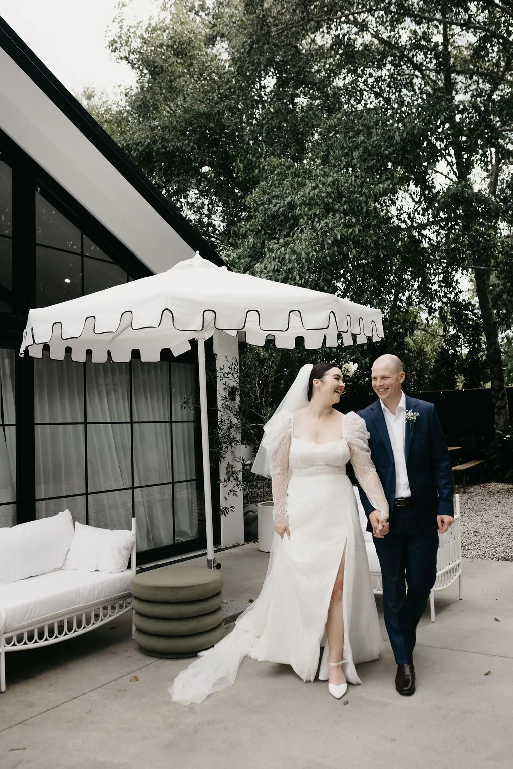Chloe and Mitchell walking together at Six One Five Matakana under a striped umbrella