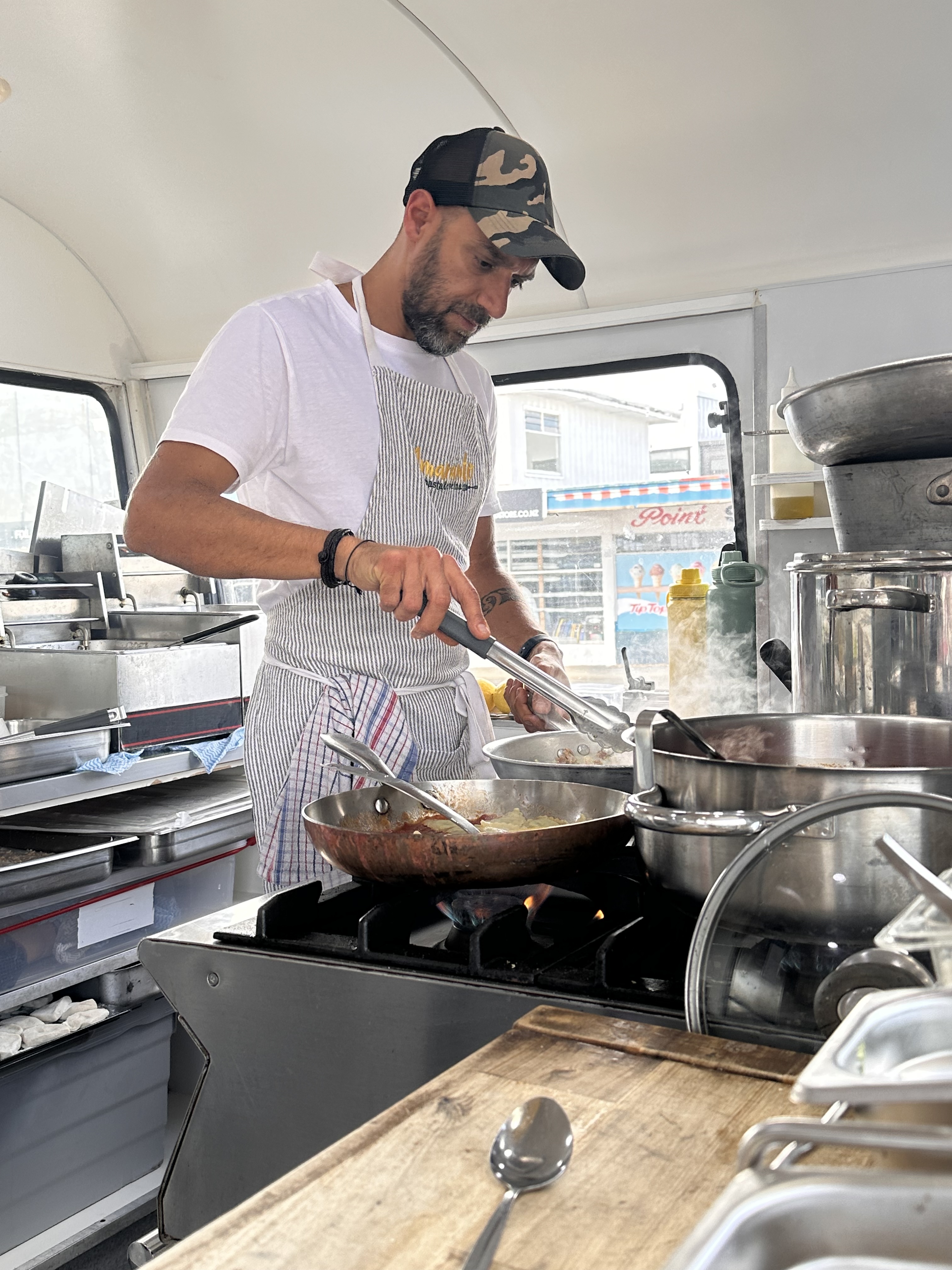 Tommaso, chef and co-founder of Amaranto, cooking fresh pasta inside the vintage caravan kitchen with flames on the gas stove