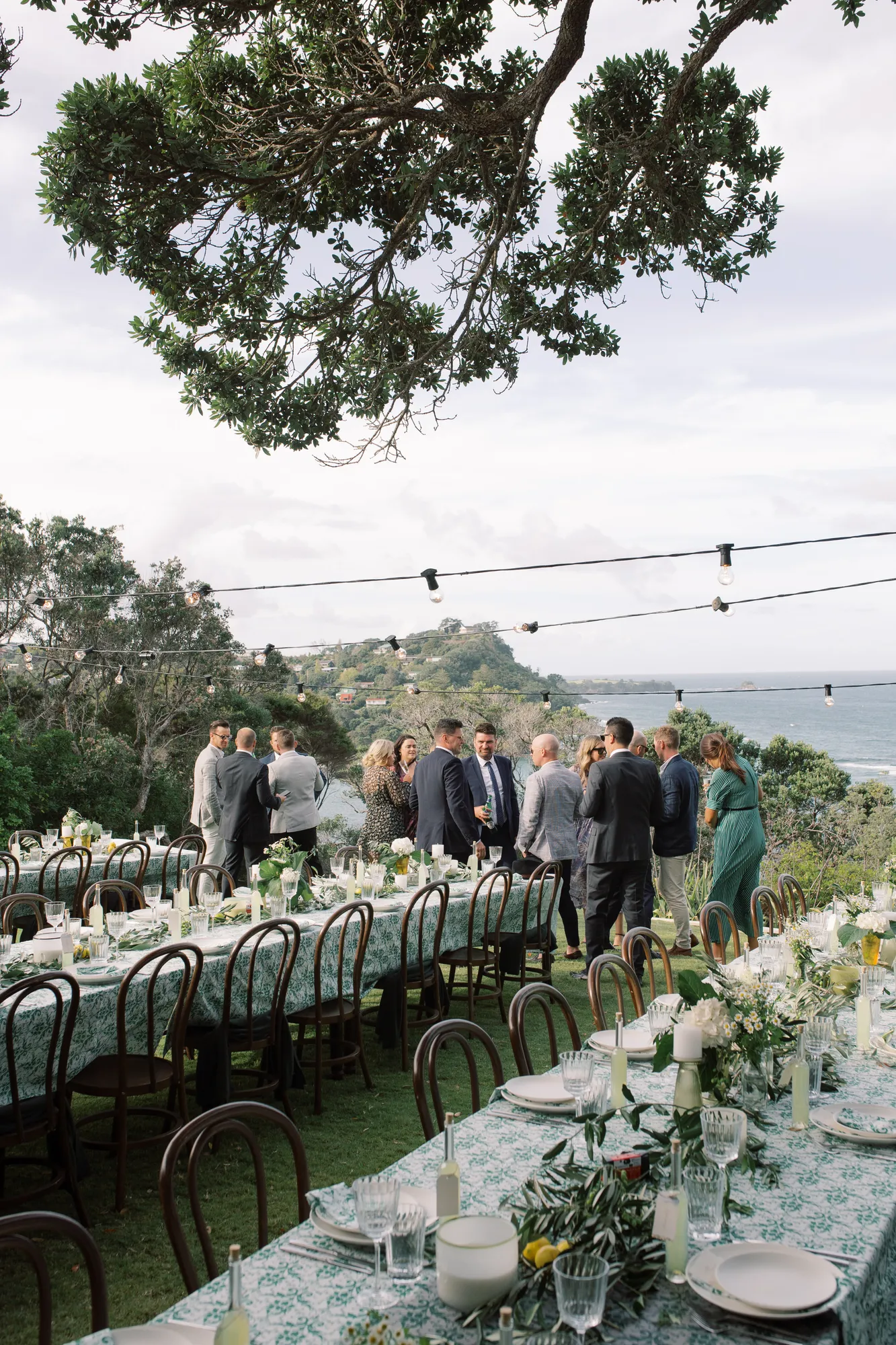 Elle and Sam walking between the long dining tables with the ocean stretching behind them at Ti Point