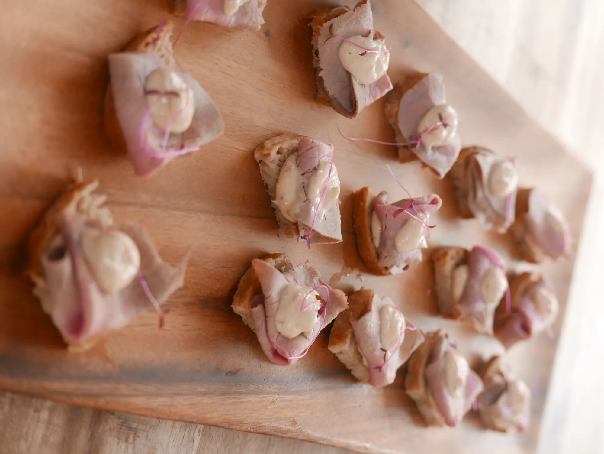 Vitello Tonnato canapés arranged on a wooden board at Elle and Sam's wedding at Ti Point
