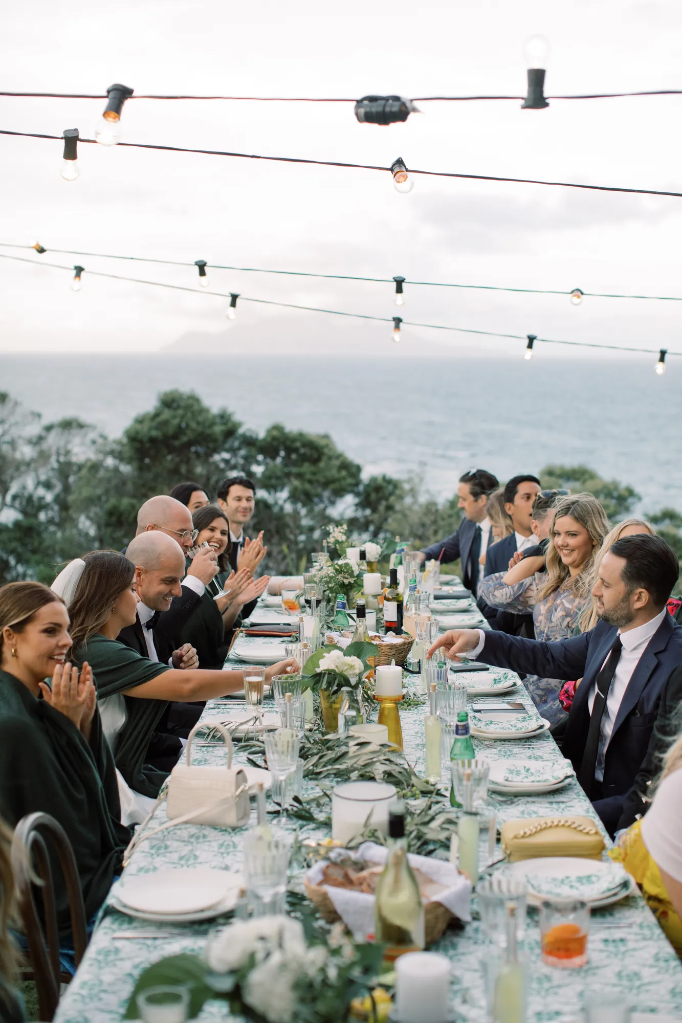 Guests laughing together at the long dining tables at Elle and Sam's wedding at Ti Point
