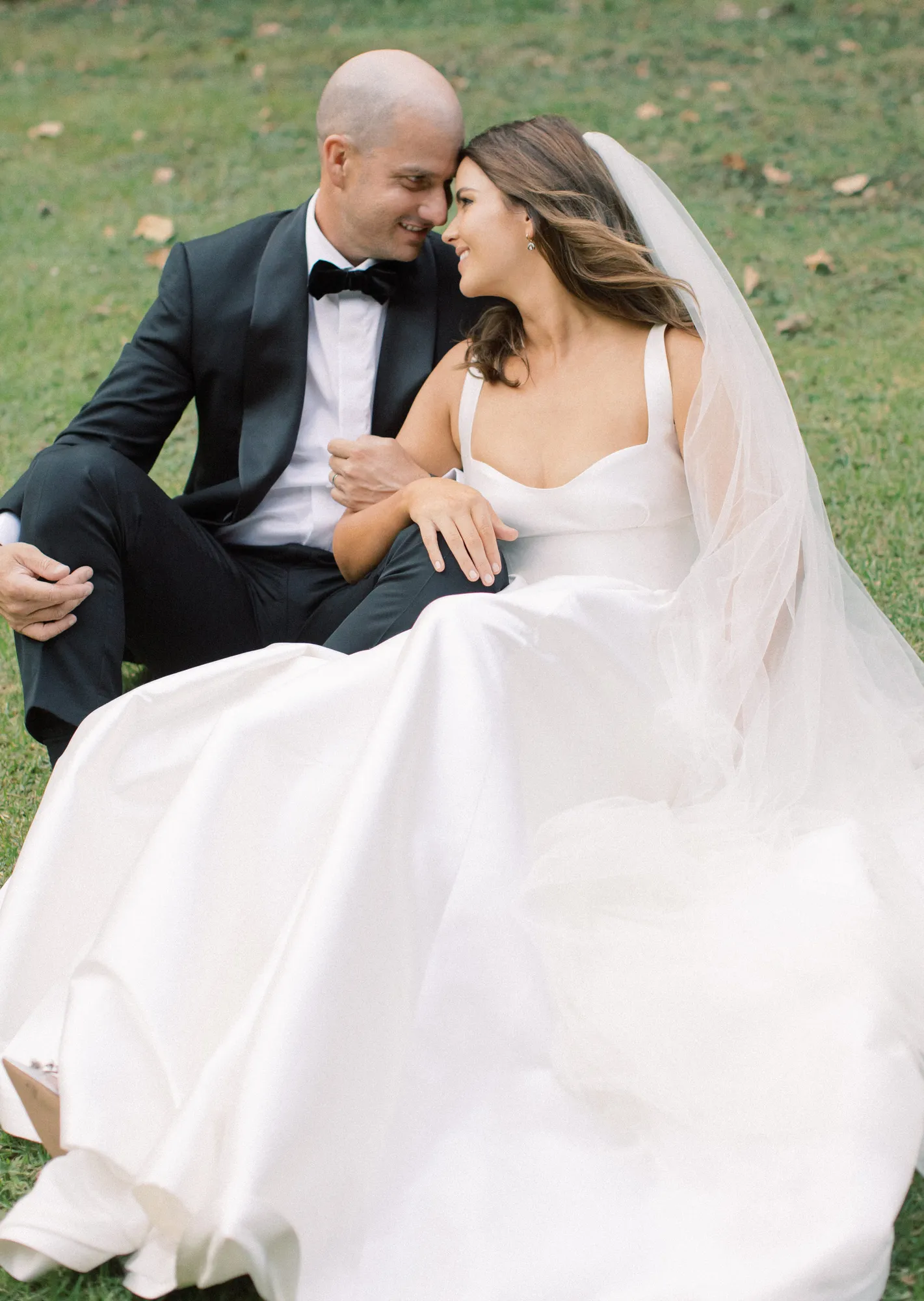 Elle and Sam sitting on the grass looking at each other at their Ti Point wedding