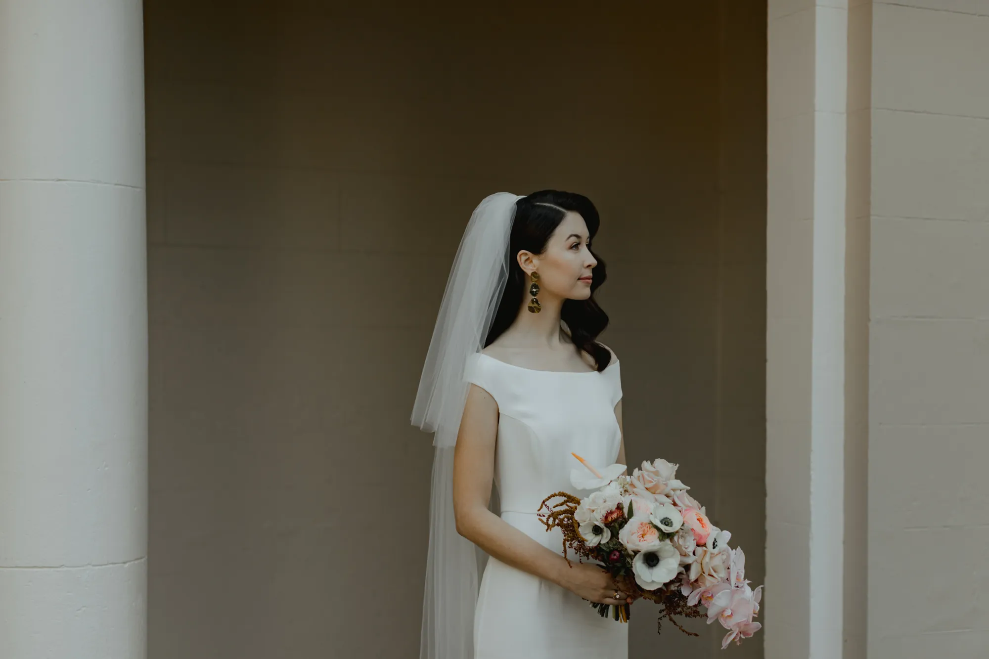 Lily in profile against a white column, holding a blush and white bouquet