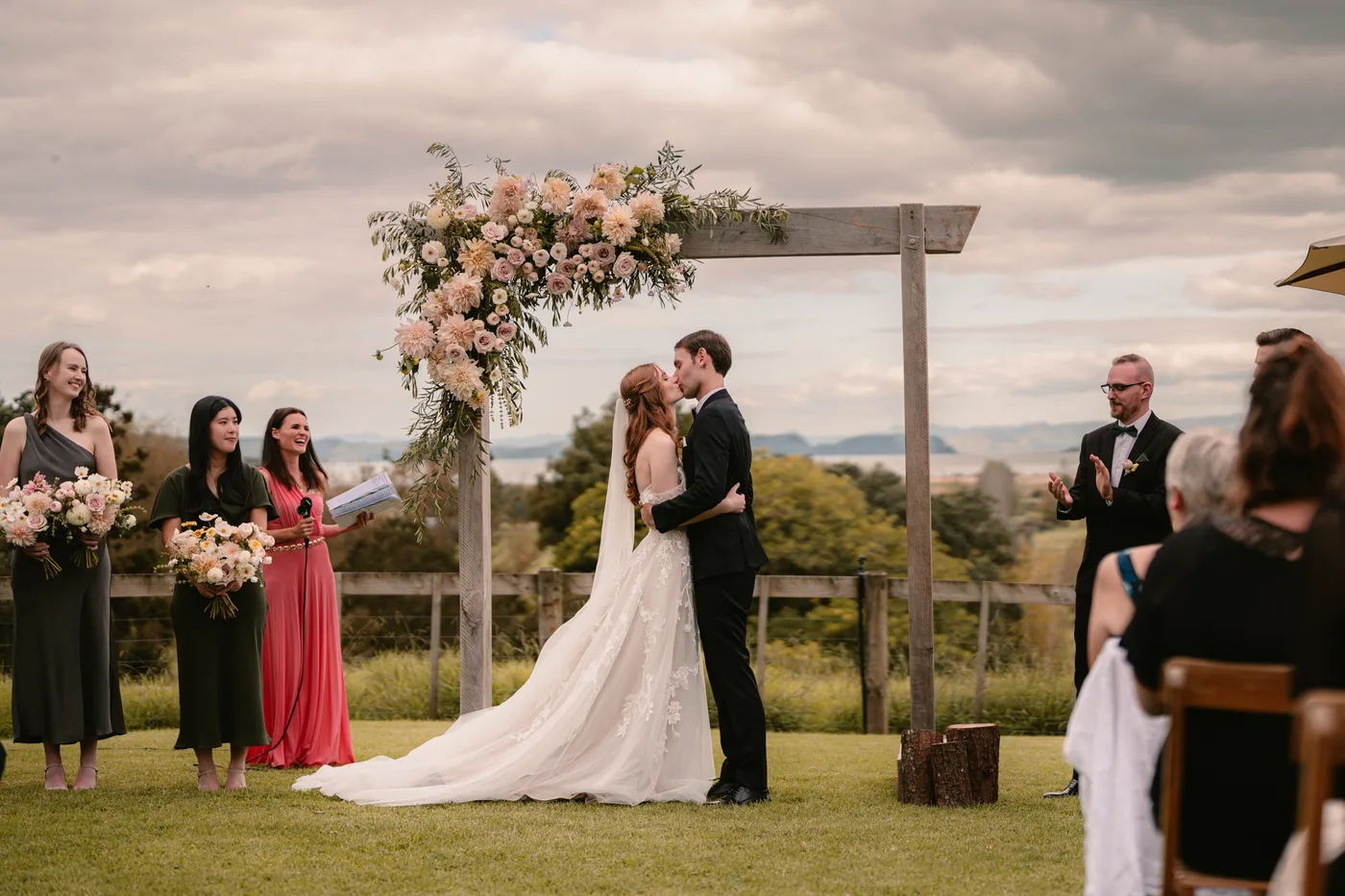 Tim and Courtney share their first kiss under the floral arch at Nocton Woolshed, with a sweeping Northland landscape behind them