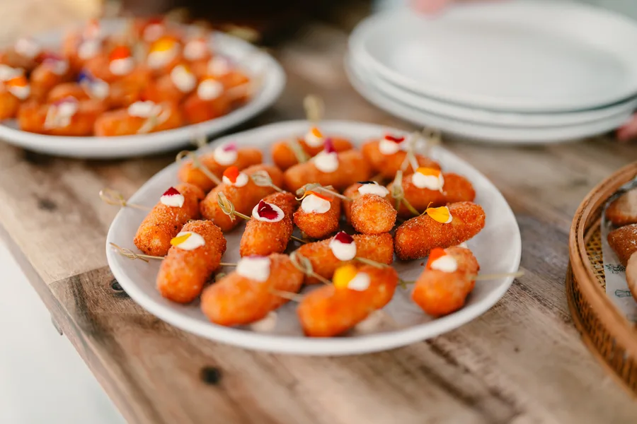 Potato and mozzarella croquettes with edible flowers on toothpicks, arranged on a white plate on a rustic timber board