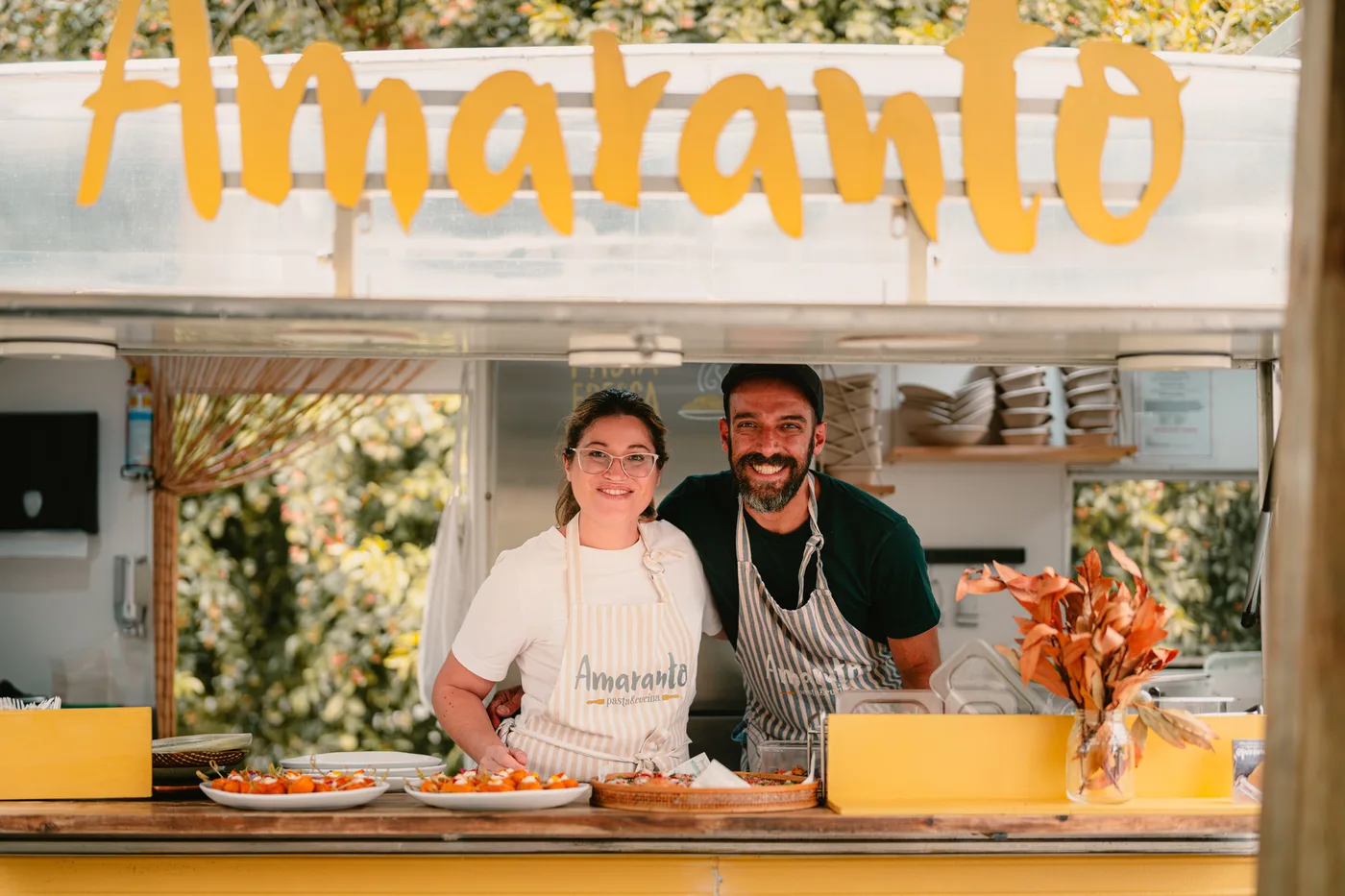 Luisa and Diego from Amaranto Pasta & Cucina smiling behind the caravan counter, ready to serve fresh pasta