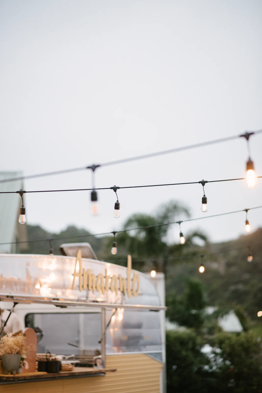 The Amaranto caravan glowing softly under festoon lights at dusk at Sandi and Ryan's wedding, Whangaumu Bay