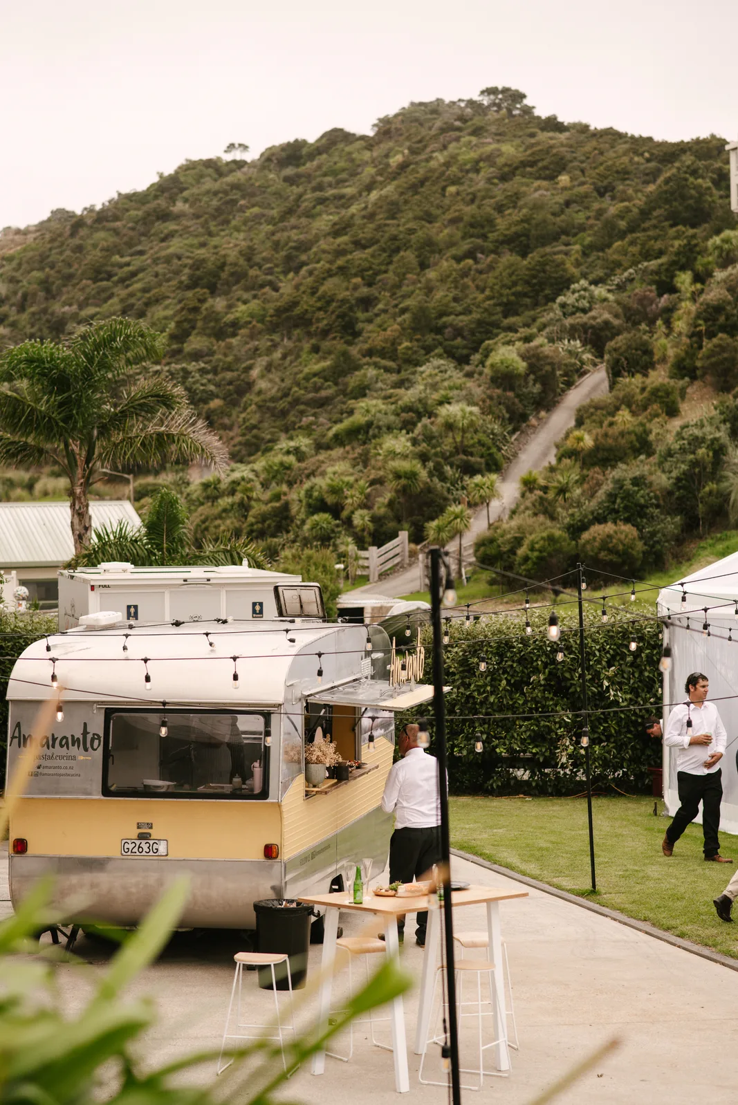 Wide shot of the Amaranto caravan set up at Whangaumu Bay with the Northland hills stretching behind, at Sandi and Ryan's wedding on the Tutukaka Coast
